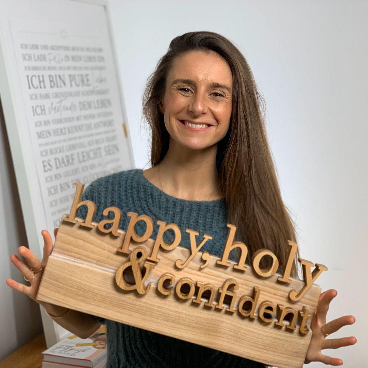 Laura Marlina Seiler hält das handgefertigte Happy Holy Confident Holzlogo in der Hand, das ihre Videos auf YouTube seit vielen Jahren begleitet.